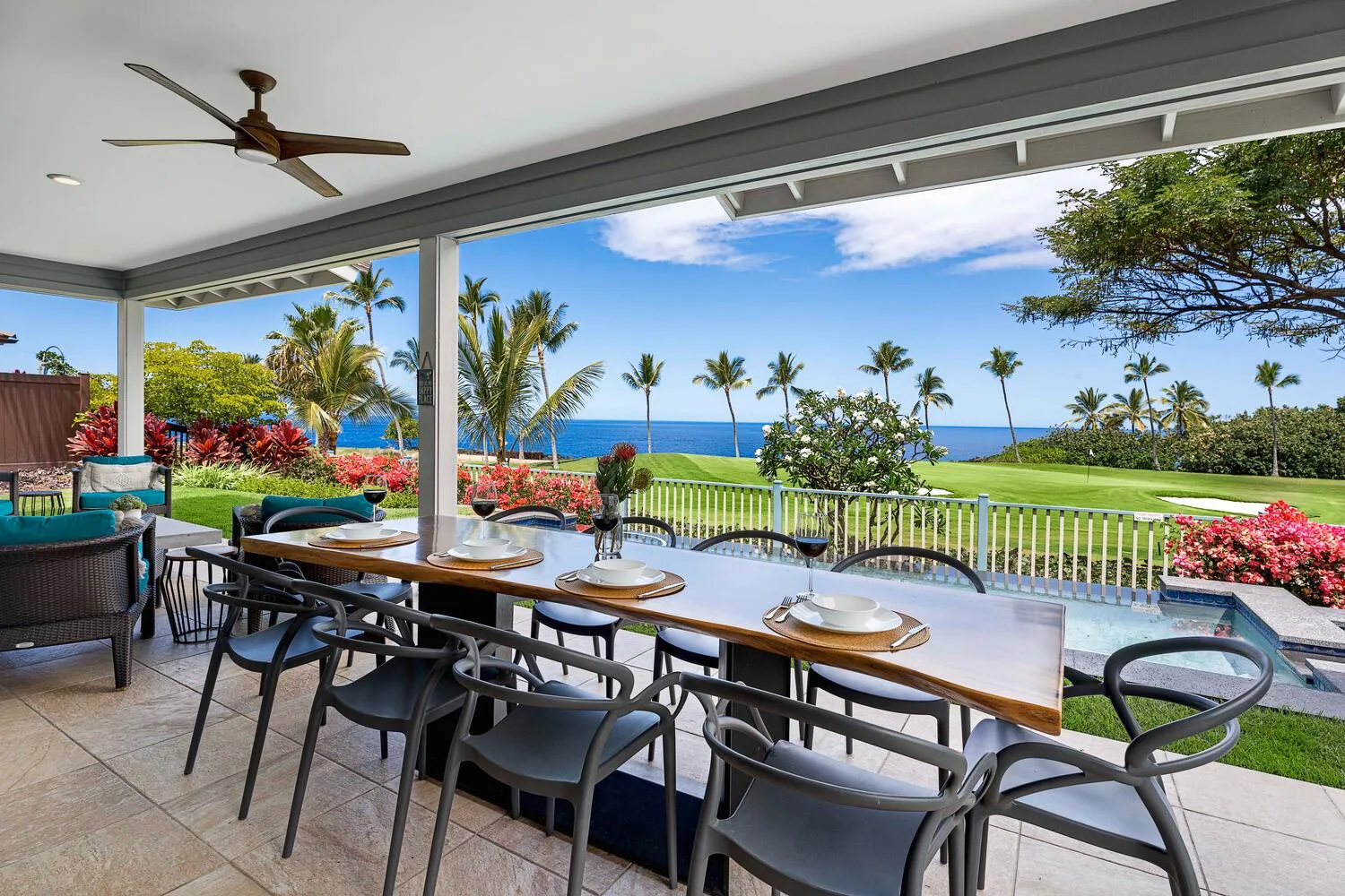 A covered outdoor dining area overlooks a green lawn, palm trees, and the ocean.