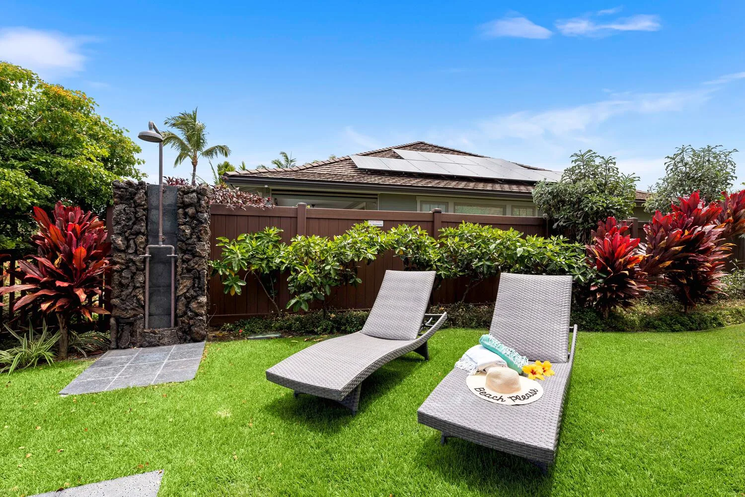 A garden patio has two lounge chairs on the lawn beside a hedge.