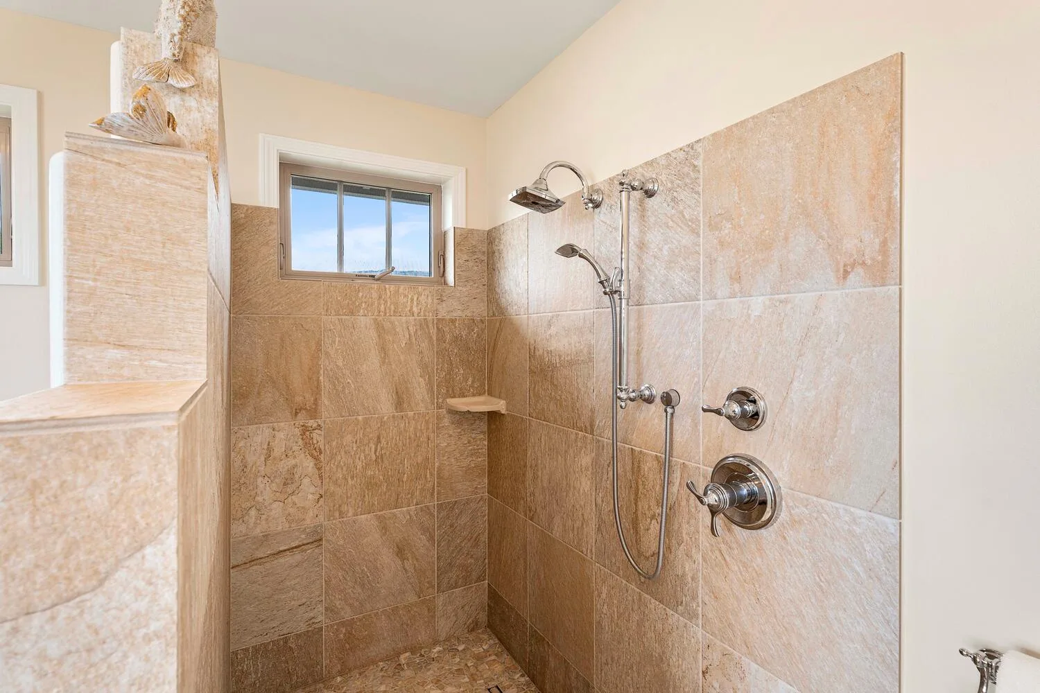 A tiled bathroom shower with a window and wall-mounted shower fixtures.