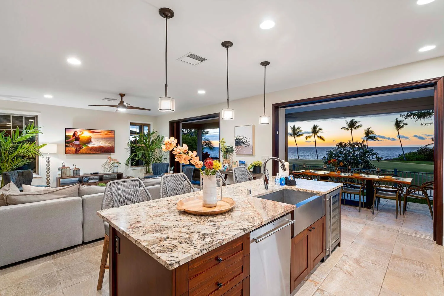 An open-plan living room and kitchen overlook a dining area and palm-lined ocean view.