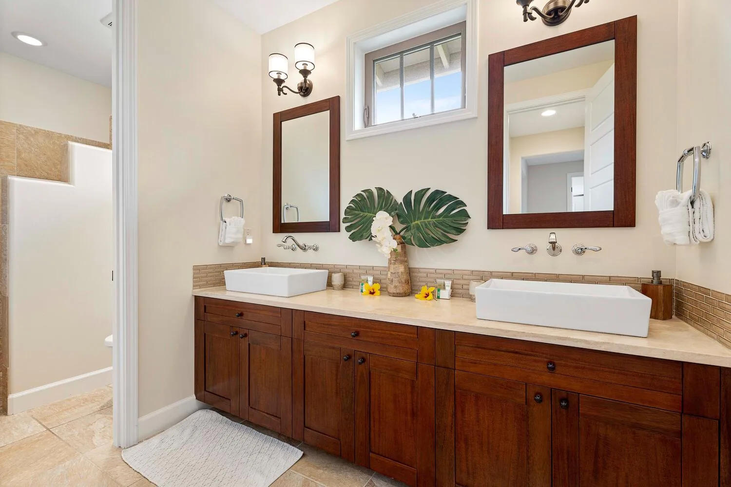 A bright bathroom features a long wooden vanity with two sinks and mirrors.