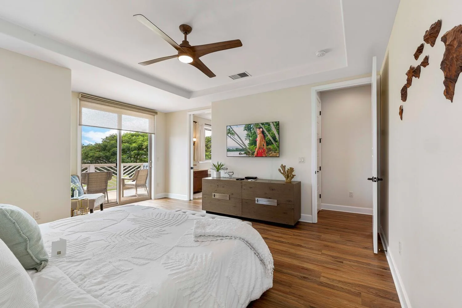 A bright bedroom with a bed, a wooden dresser, and glass doors opening to a balcony.