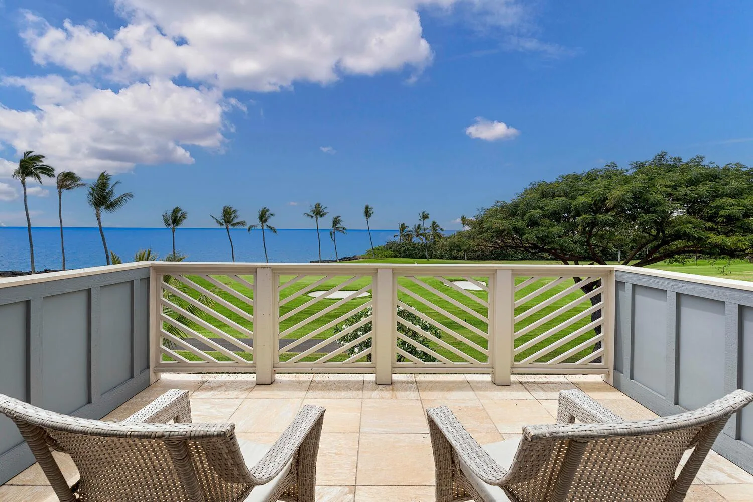 A tiled terrace overlooks a railing, palm trees, and the ocean.