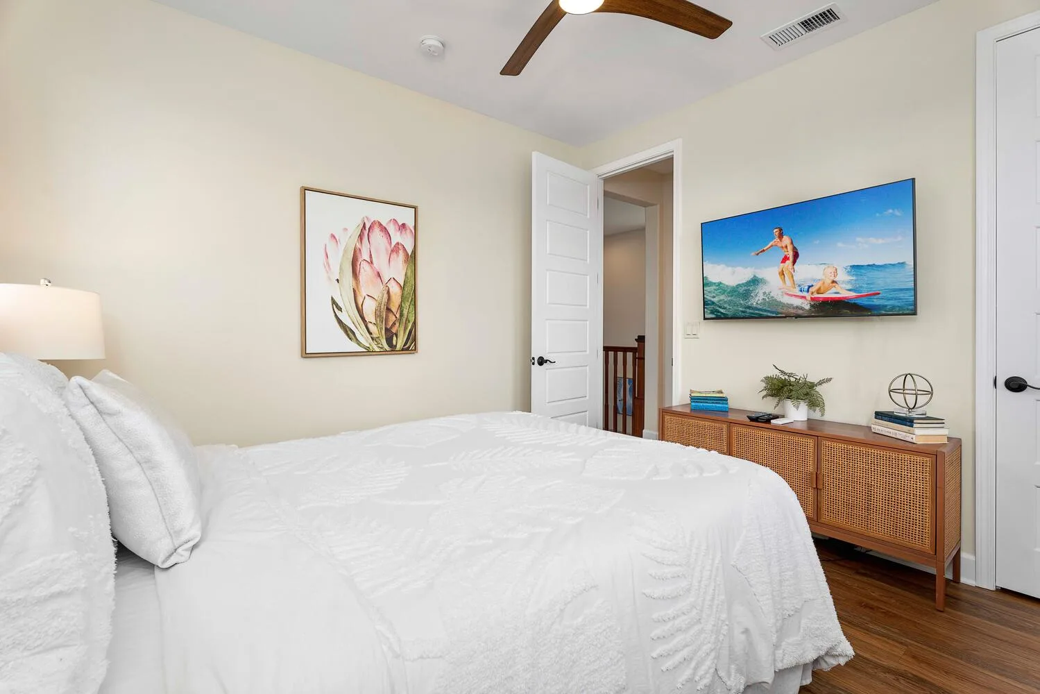 A bright bedroom with a white bed, wall-mounted television, and woven cabinet.
