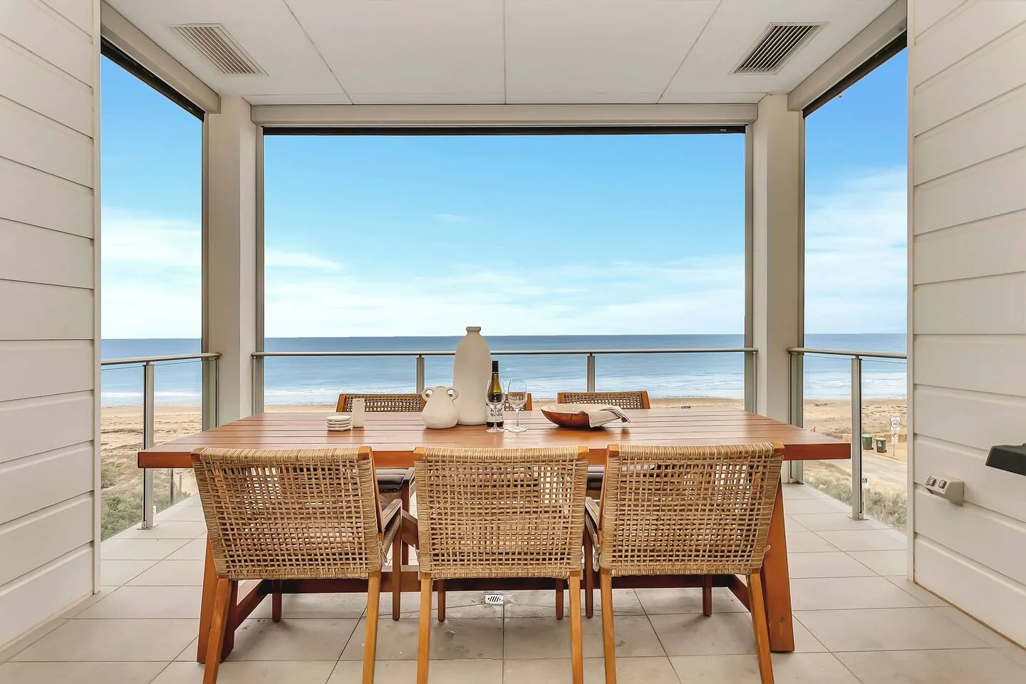 Un comedor al aire libre con una mesa de madera y asientos tejidos ofrece vistas al océano.