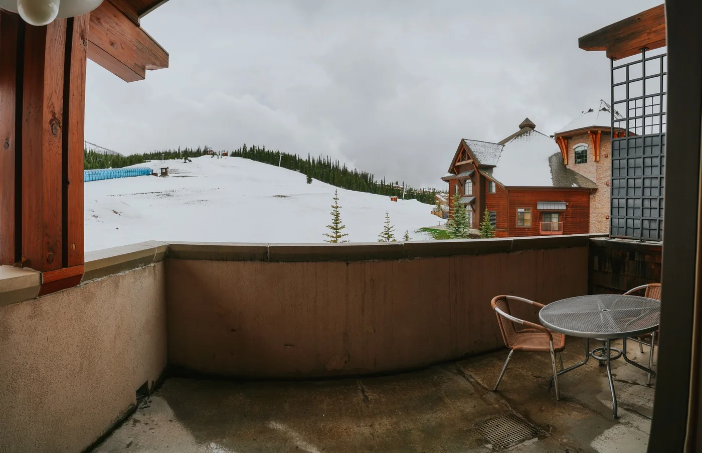 A balcony with outdoor seating overlooks a snowy hillside and nearby buildings.