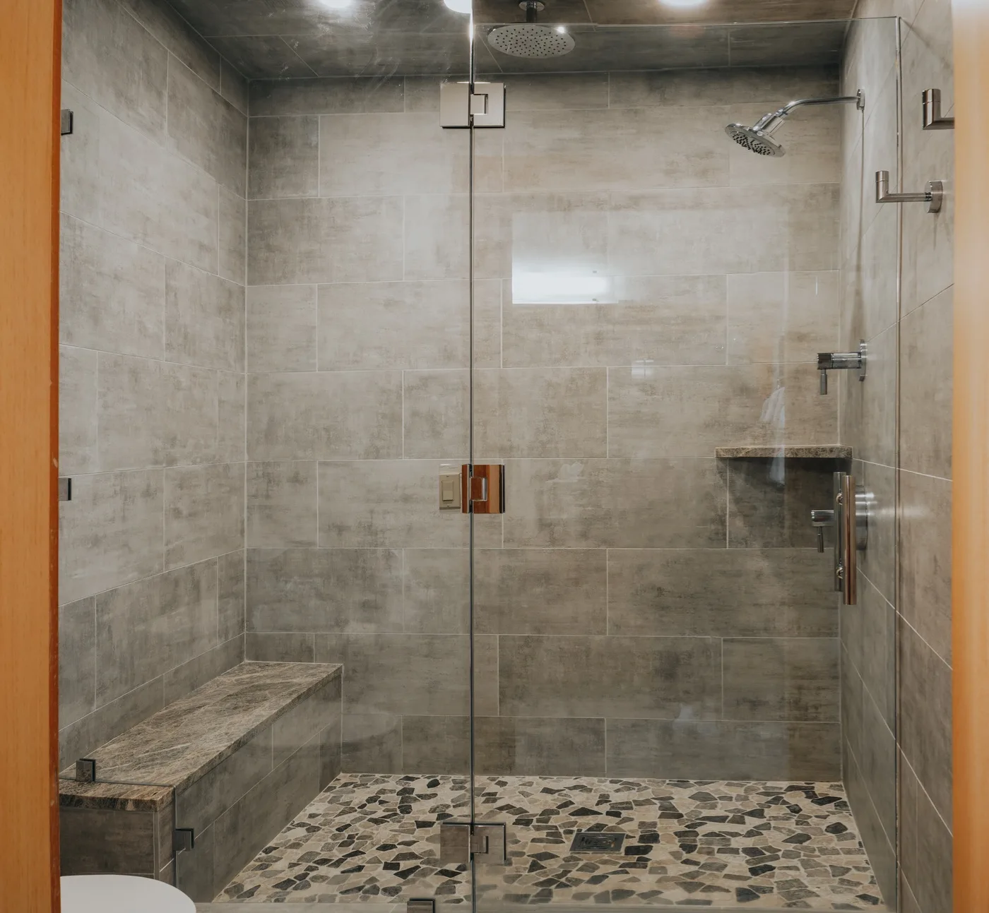 Una ducha de baño alicatada con paneles de vidrio y un banco integrado.