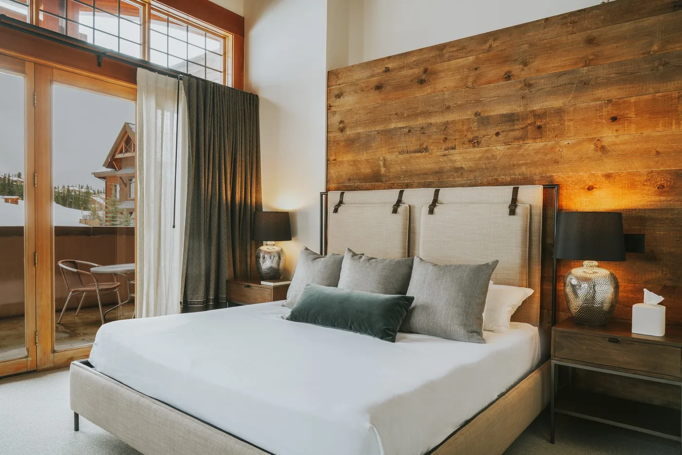 Un dormitorio con una cama bien hecha, una pared de madera y grandes puertas de vidrio.