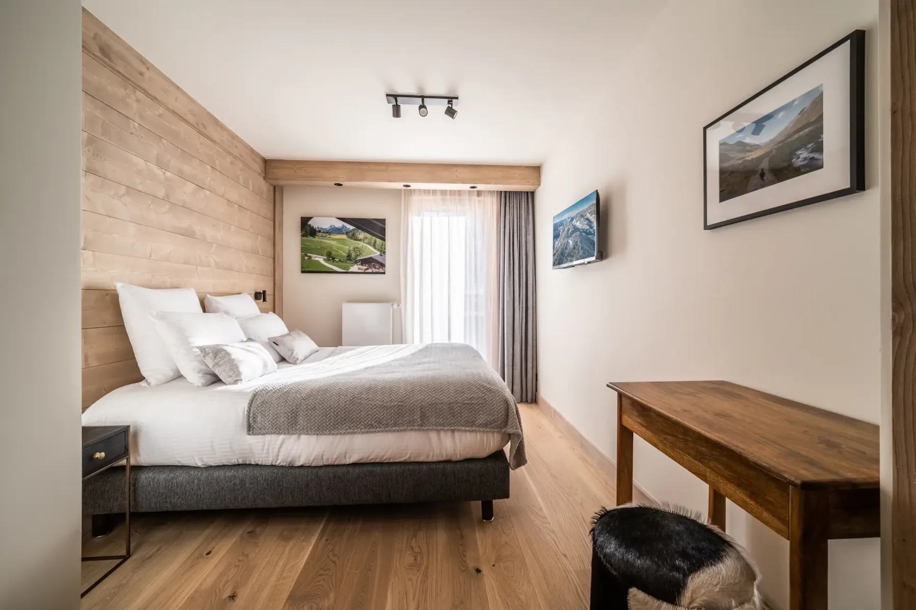 A bedroom with a double bed, wood flooring, and a desk beside the window.