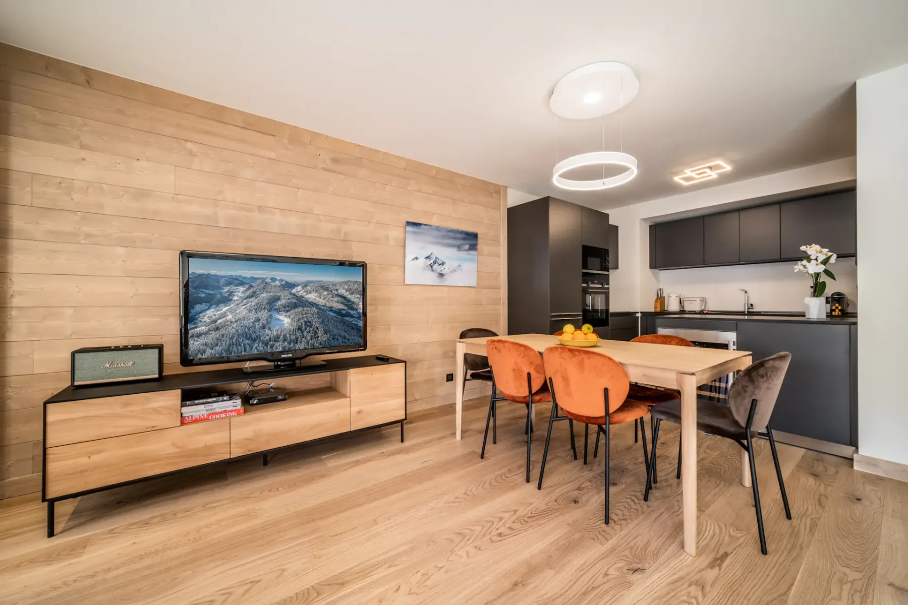 A dining table and seating sit beside a television in a modern living area.