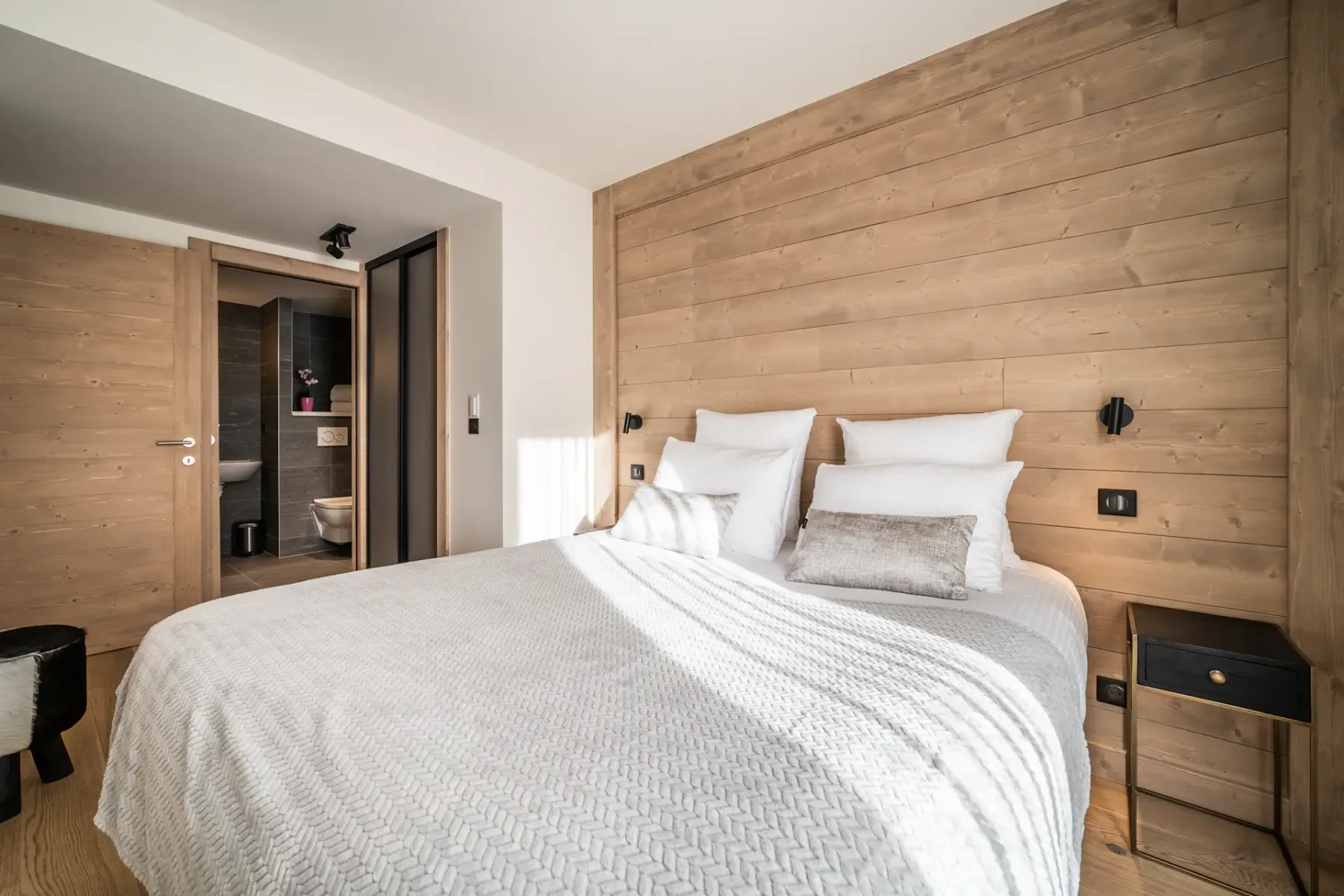 A bedroom with a double bed, white bedding, and light wood-paneled walls.