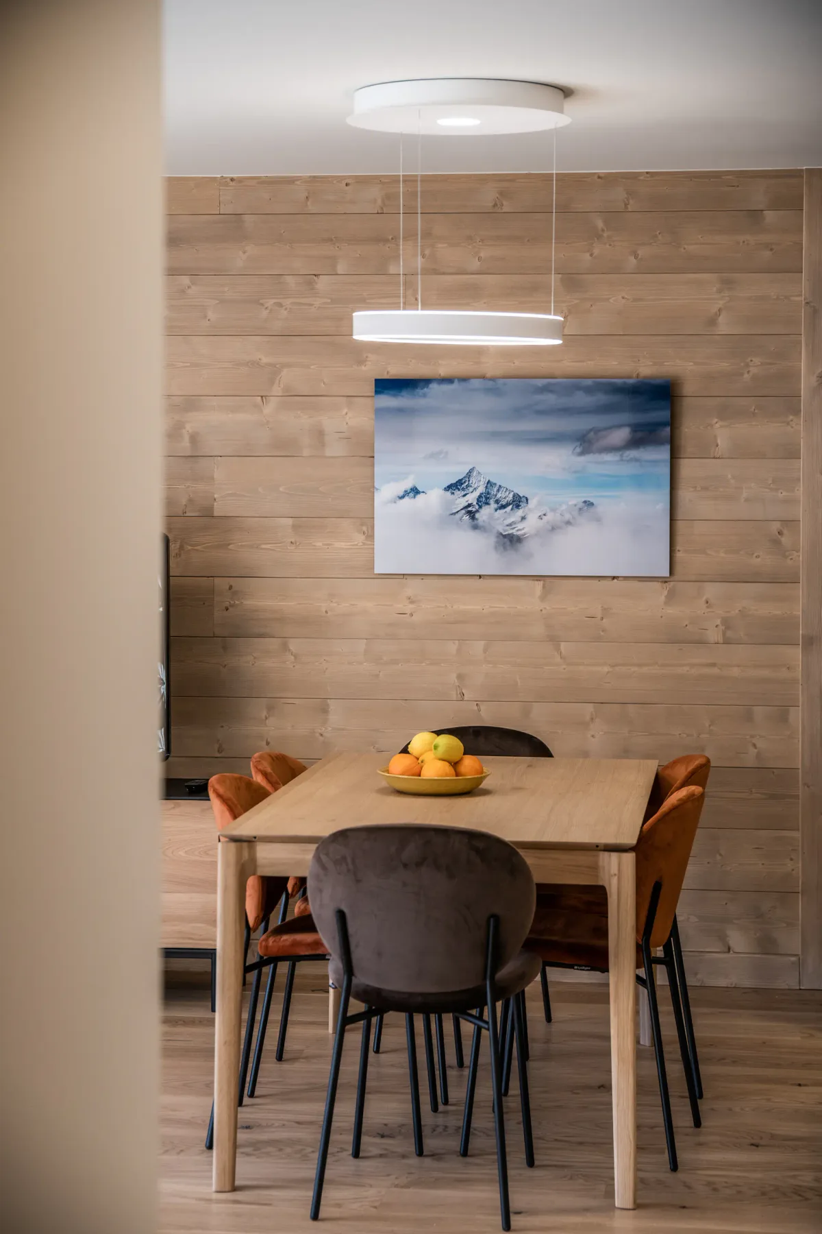 A dining area with a wooden table and a mountain picture on the wall.