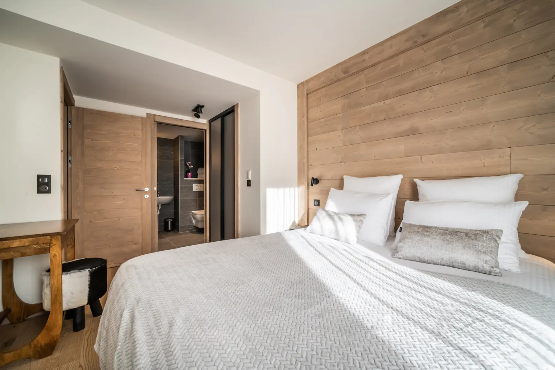 A bedroom with a neatly made bed and an open doorway to the bathroom.