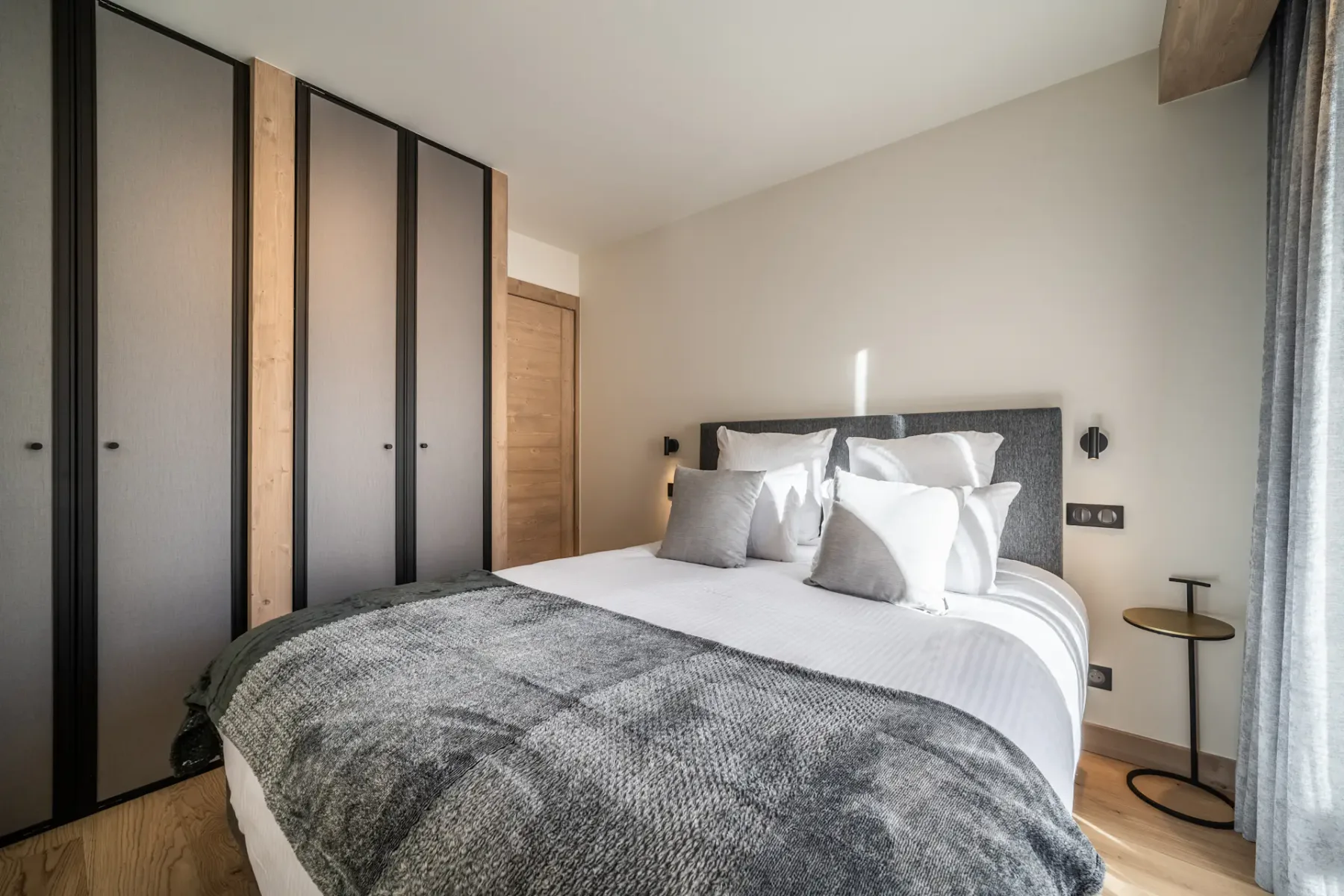 A bedroom with a double bed, gray headboard, and built-in wardrobes.