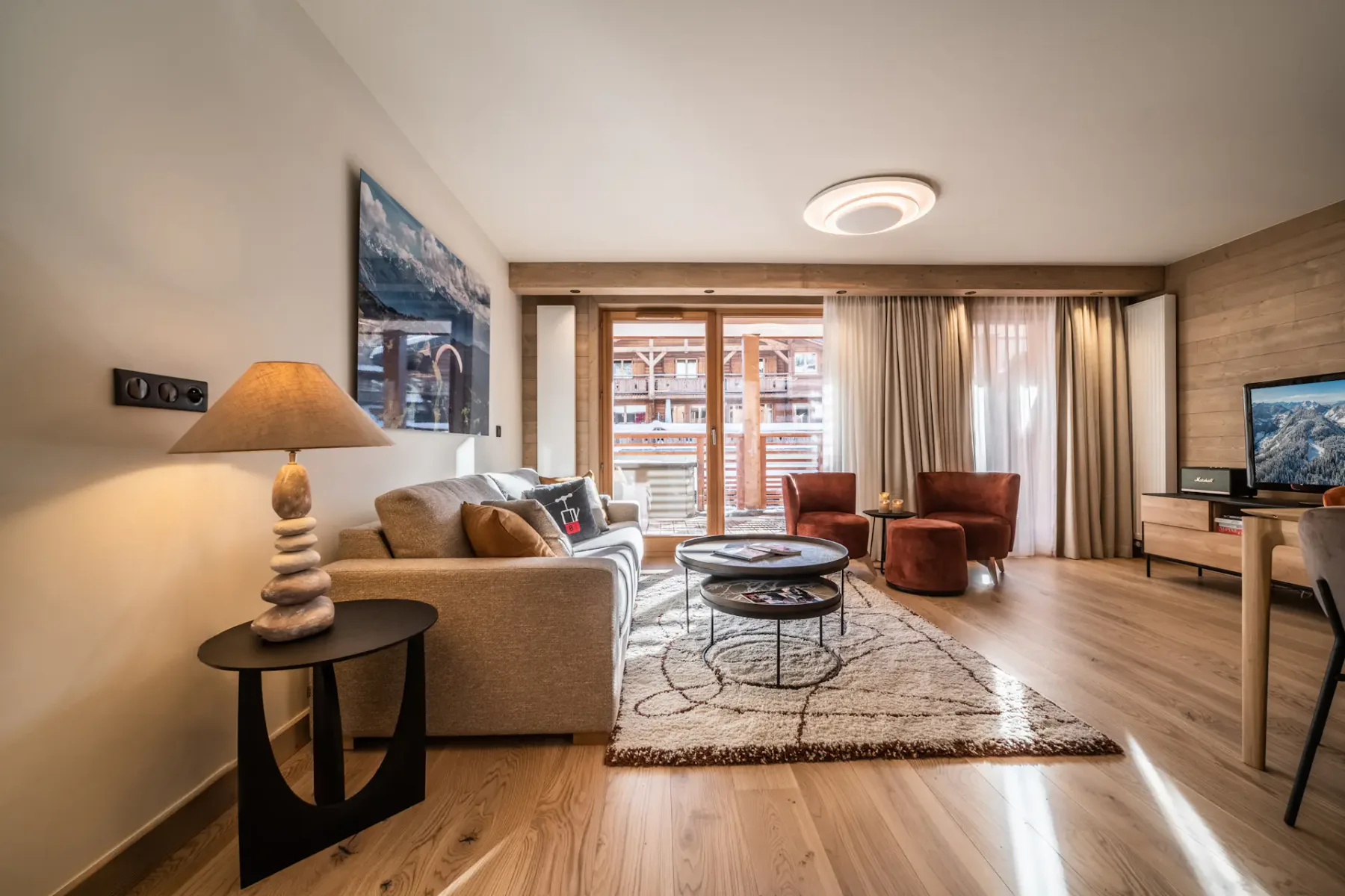 A living room with seating, a rug, and a coffee table beside large windows.