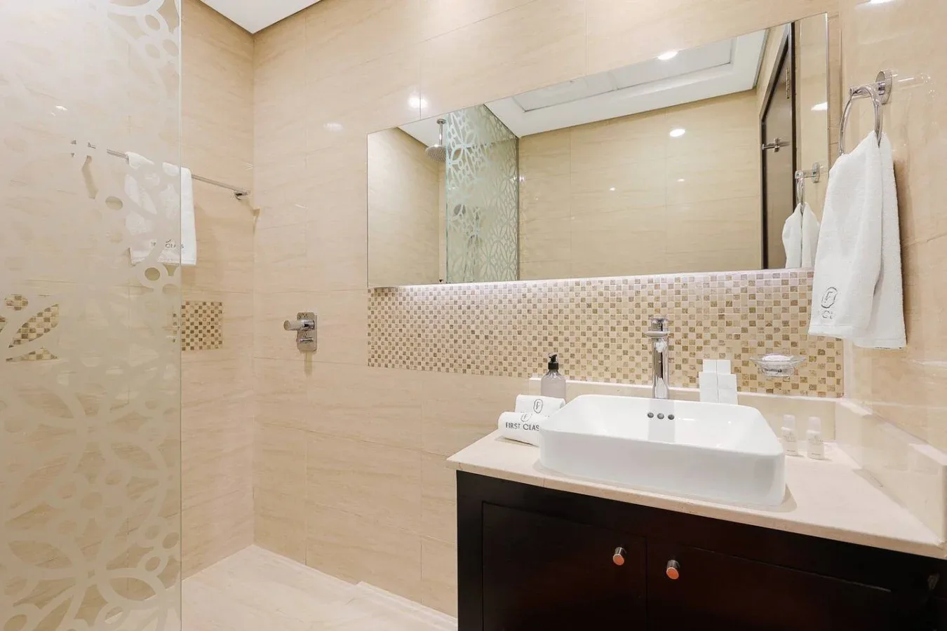 Un baño revestido de azulejos con lavabo, espejo y toallas colgadas.