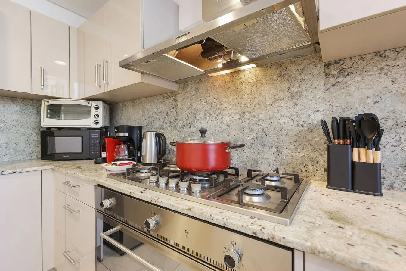 Una zona de cocina con una estufa de gas, una olla roja y electrodomésticos sobre la encimera.