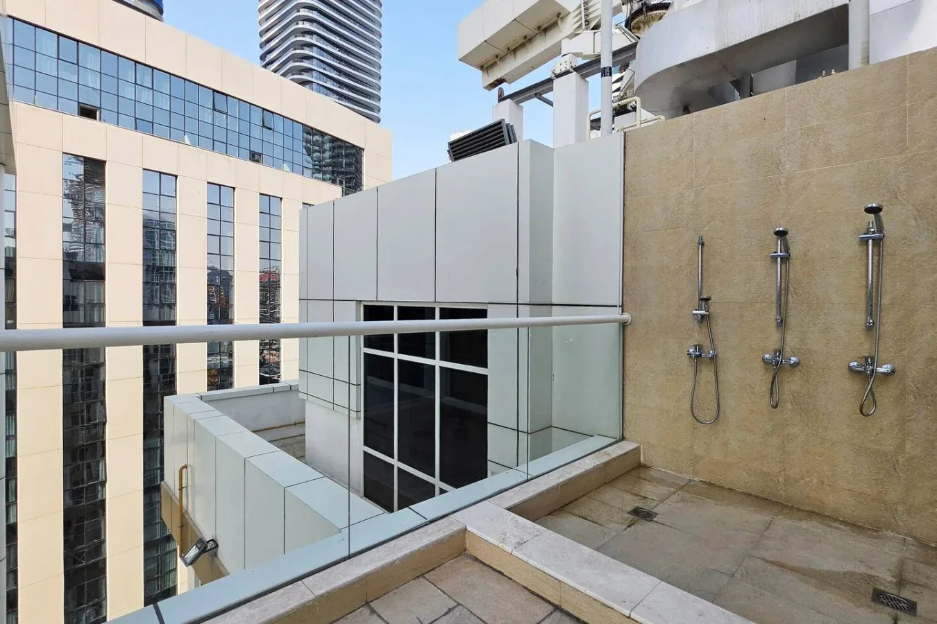 Una zona de duchas al aire libre con barandillas de vidrio y edificios altos alrededor.