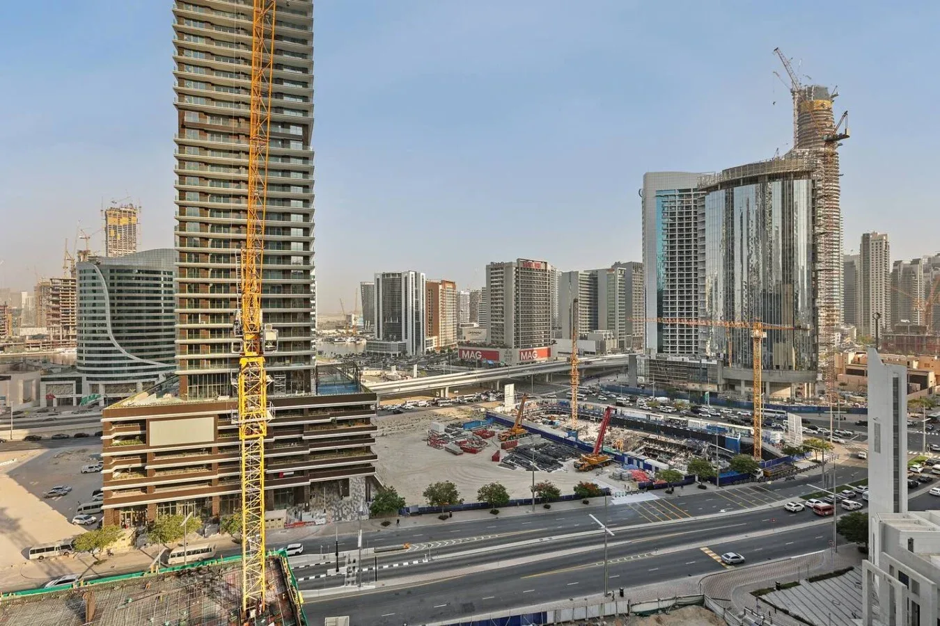 Obra urbana con grúas y edificios altos junto a una carretera transitada.