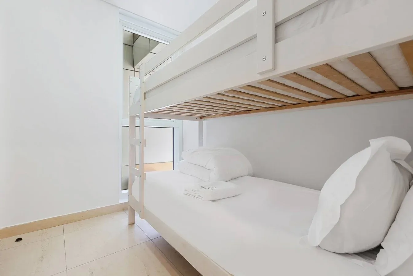 Un dormitorio con una litera blanca y ropa de cama ordenada.