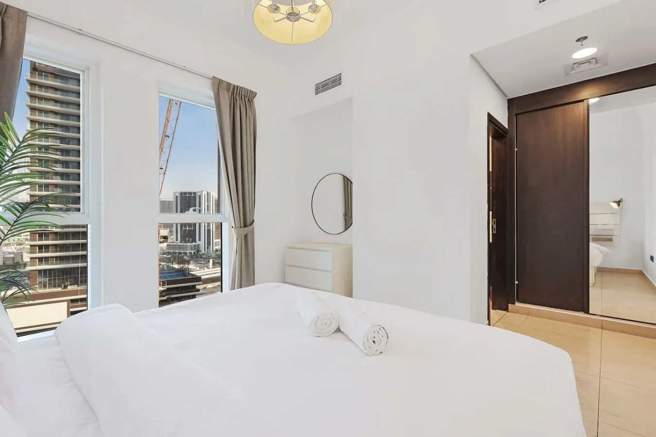 Un dormitorio luminoso con una cama blanca, ventanas altas y un armario.