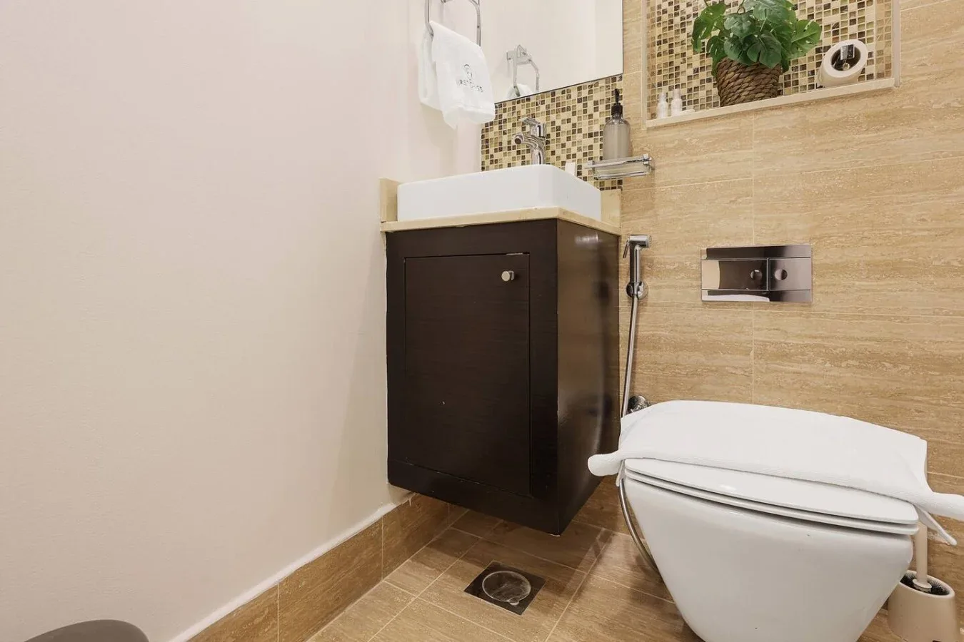 Un baño con un mueble oscuro, lavabo blanco e inodoro.