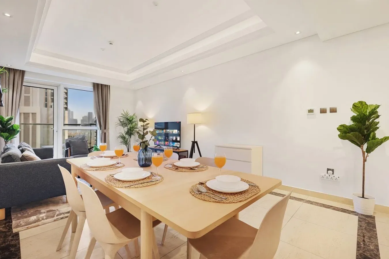 Comedor con una mesa larga puesta con platos y vasos junto a grandes ventanas.