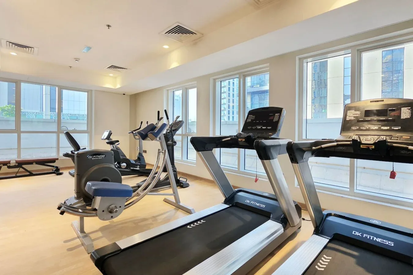 Un gimnasio con cintas de correr y otros equipos de ejercicio junto a grandes ventanas.