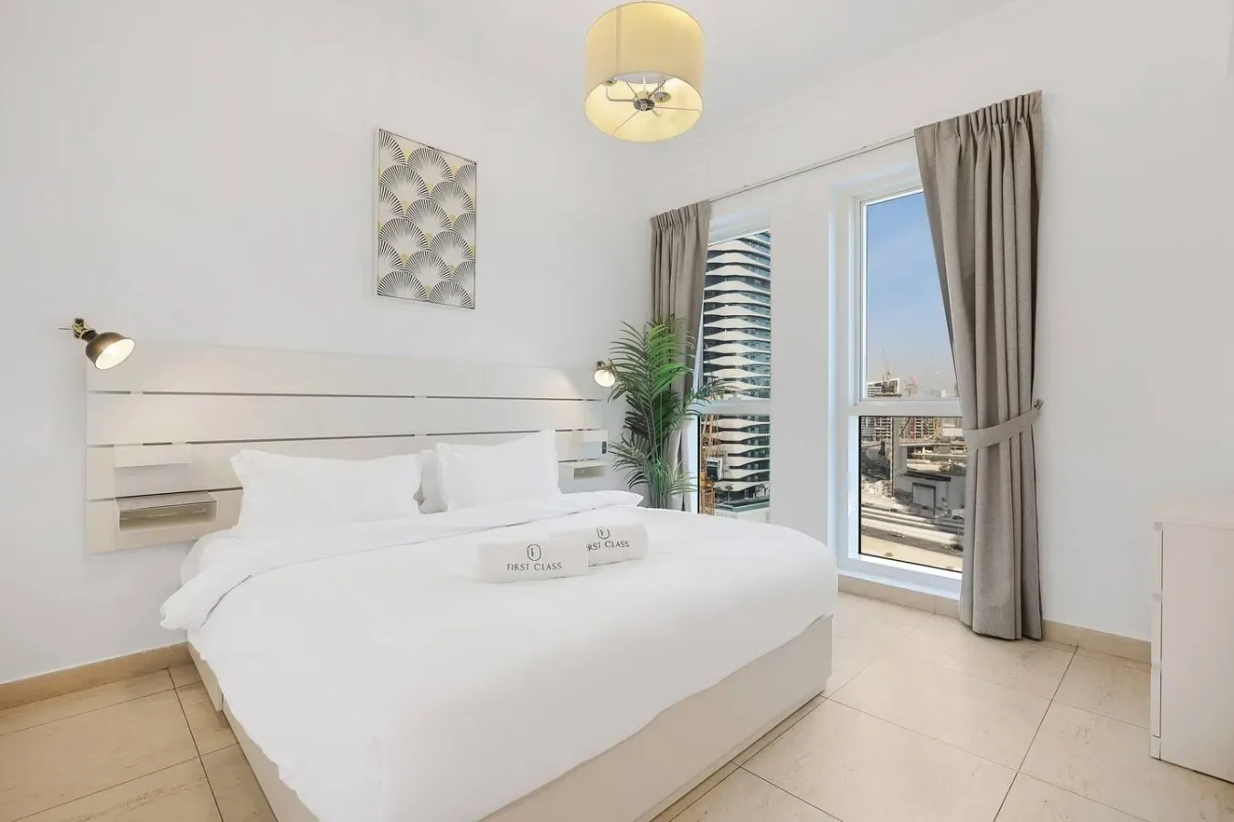 Un dormitorio luminoso con una cama bien tendida junto a una ventana alta.