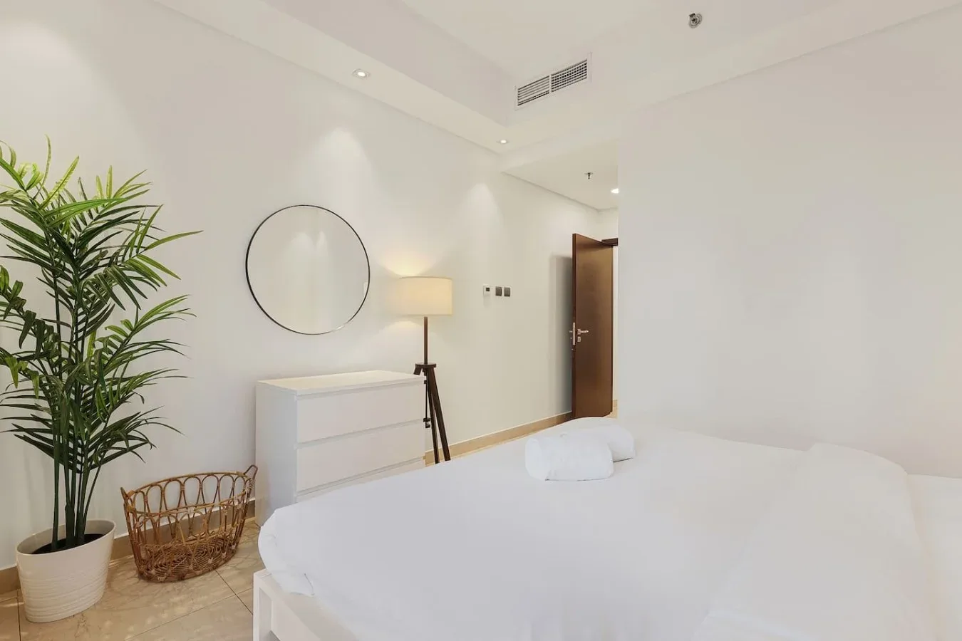 Un dormitorio luminoso con una cama bien tendida, una cómoda y una planta alta en maceta.