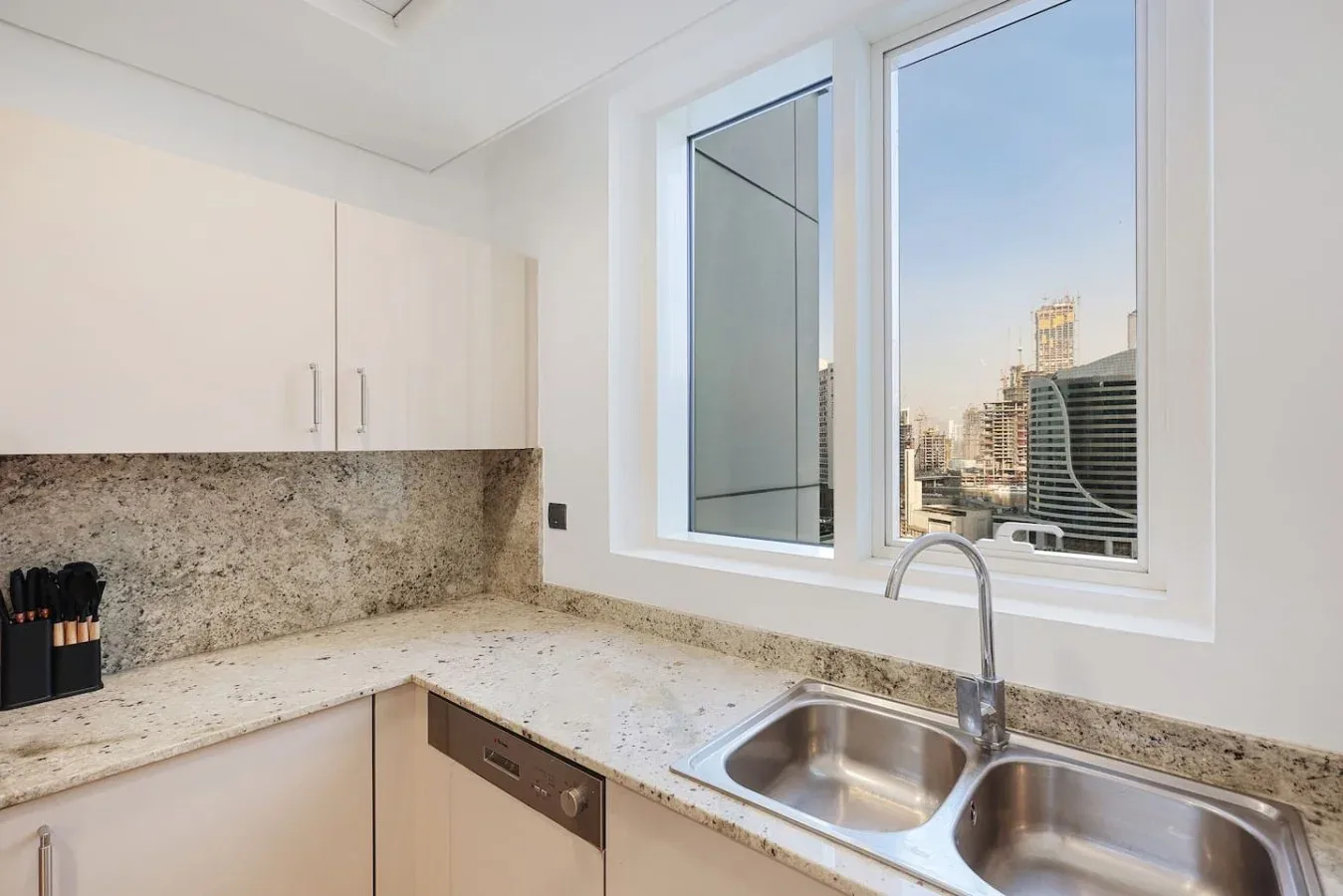 Una cocina luminosa con encimera de patrón pétreo, fregadero y grandes ventanas.