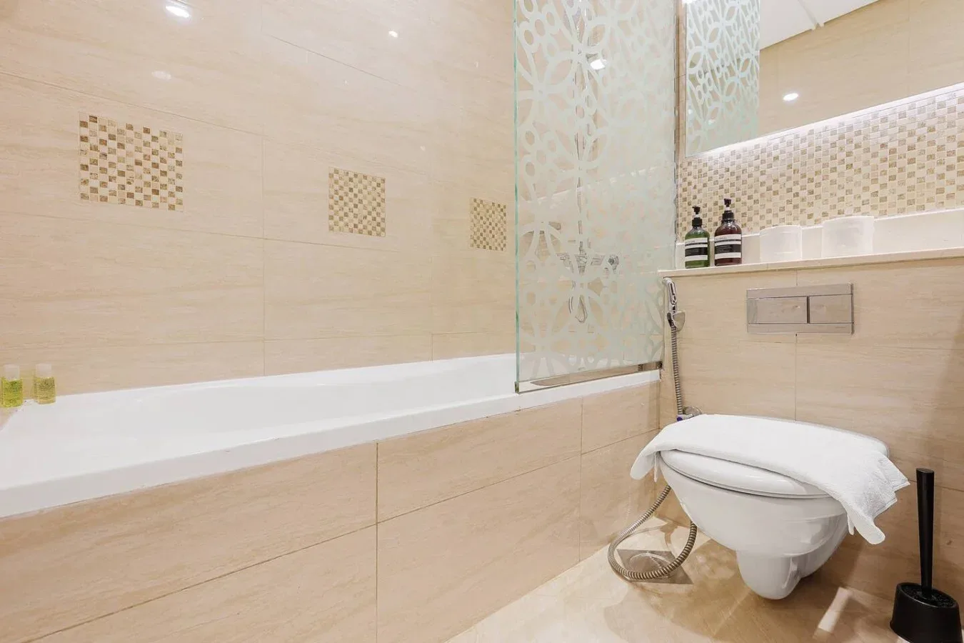 Un baño alicatado con bañera y un inodoro suspendido.