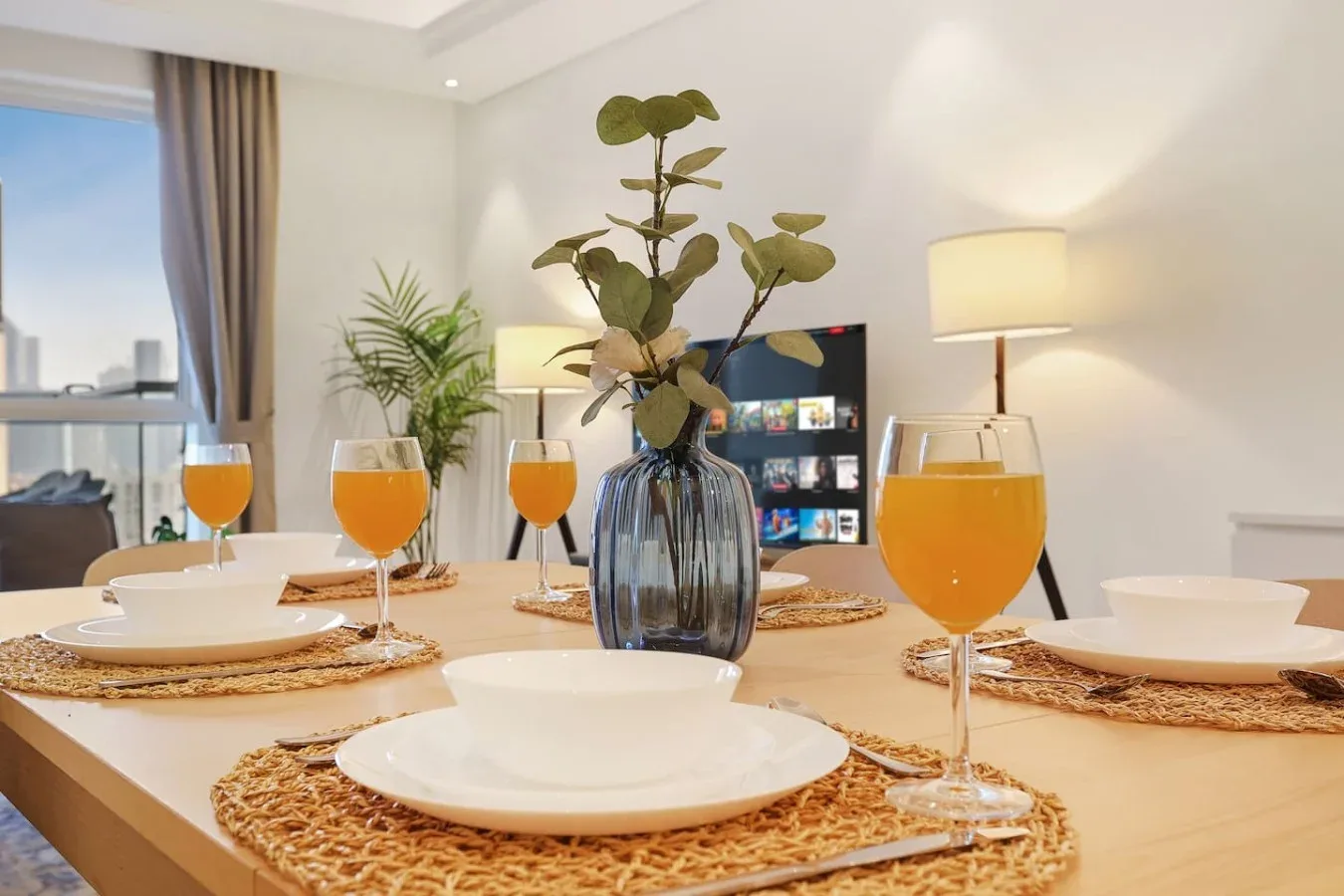 Una mesa de comedor está puesta con platos y copas en una sala luminosa.