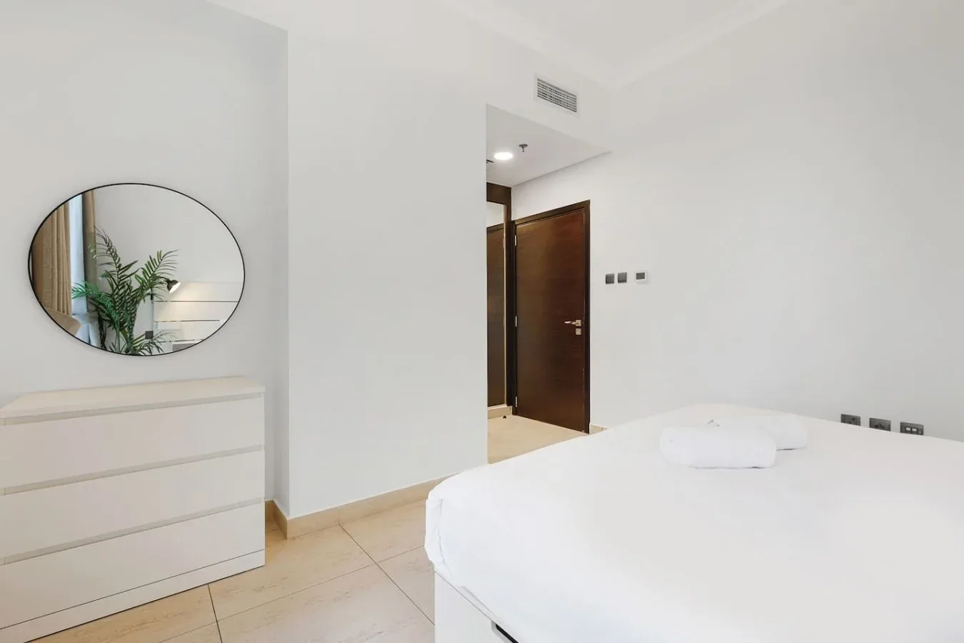 Un dormitorio luminoso con una cama blanca, una cómoda y un espejo.