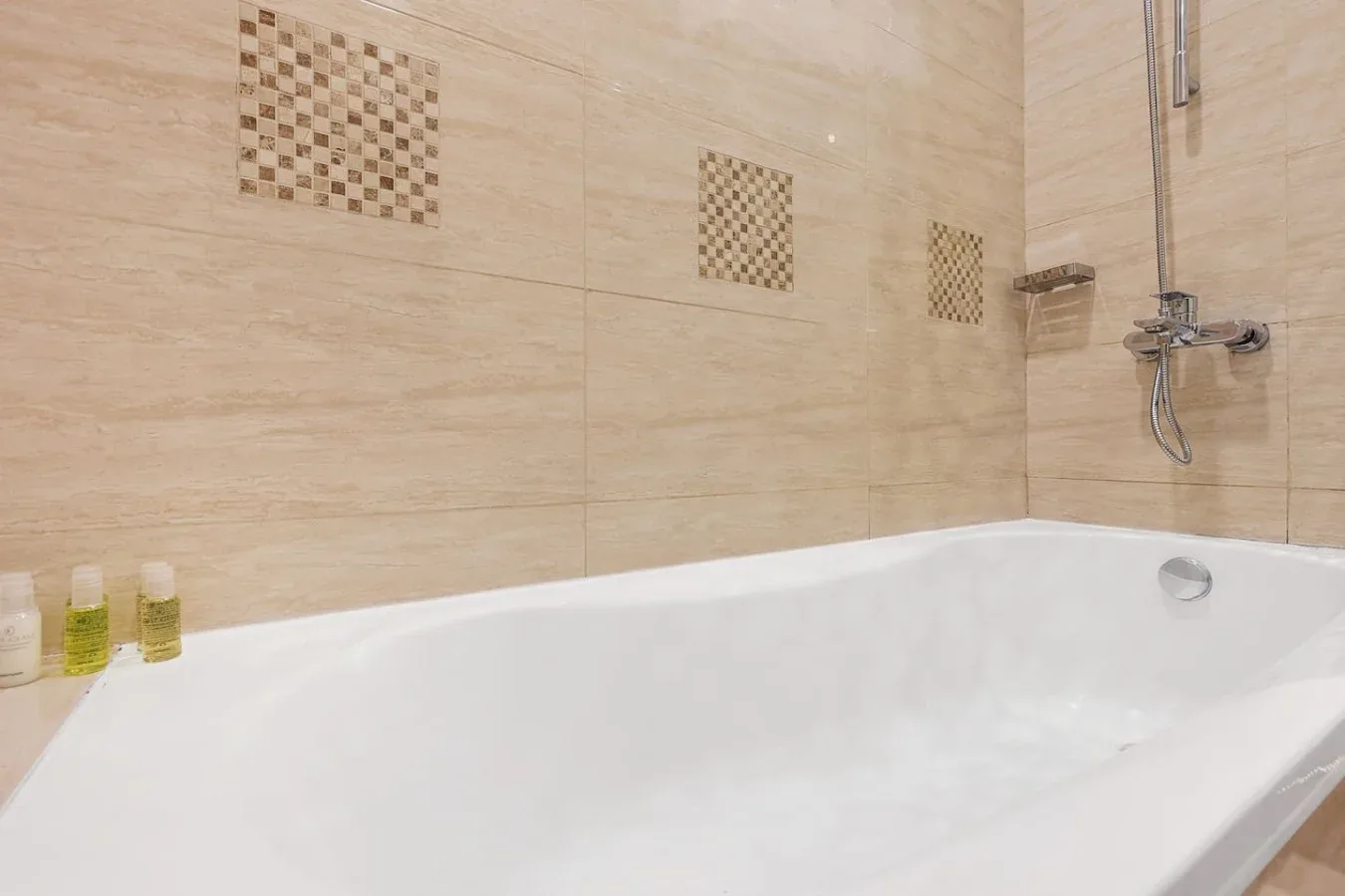 Una bañera está bajo una ducha de pared, frente a paredes revestidas con azulejos.