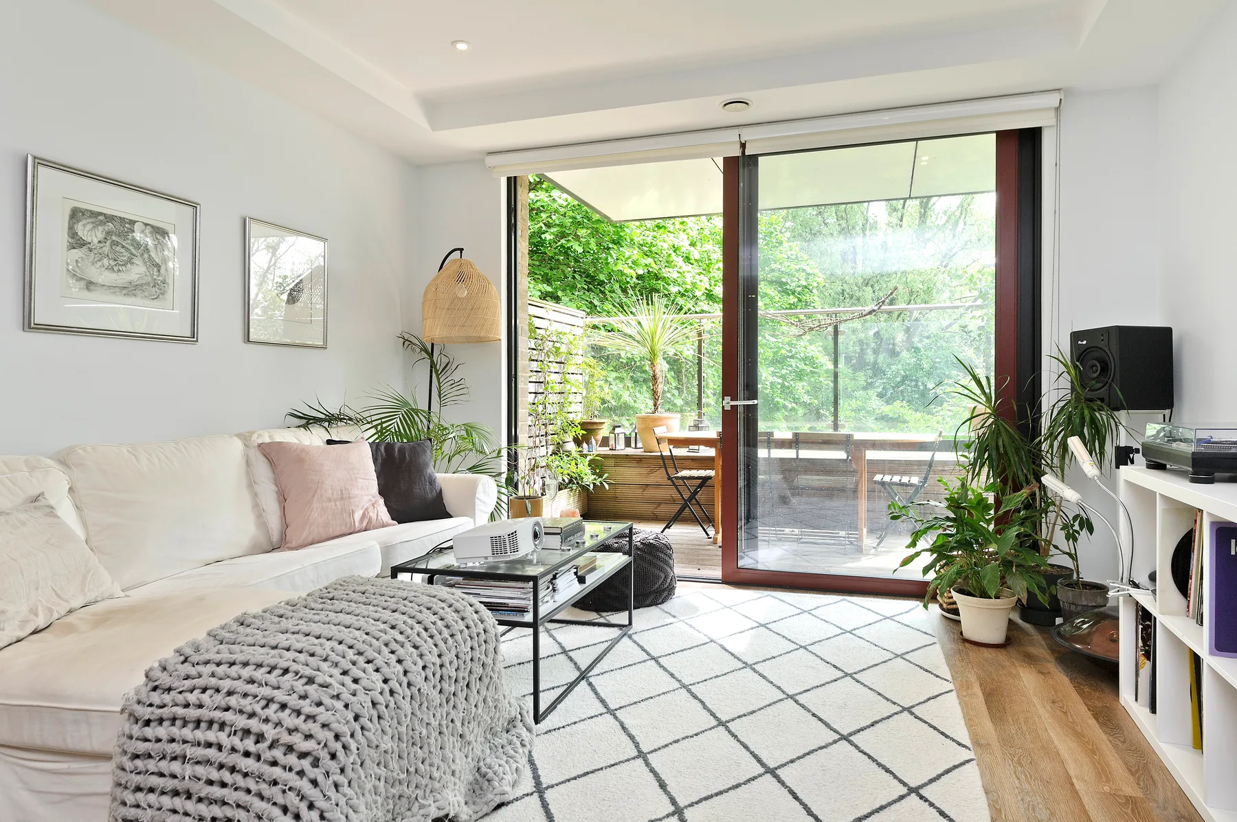 A bright living room opens onto a leafy balcony through large glass doors.