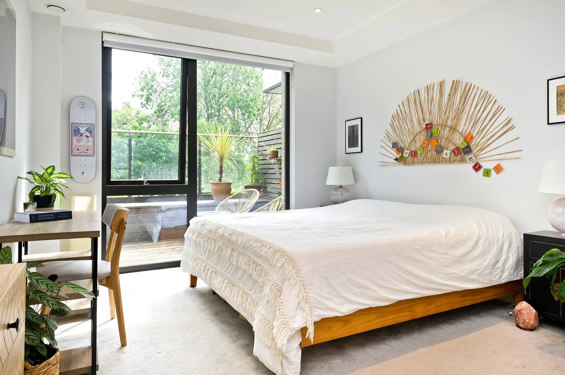 Un dormitorio luminoso con una cama junto a grandes puertas de cristal con vistas a la vegetación.
