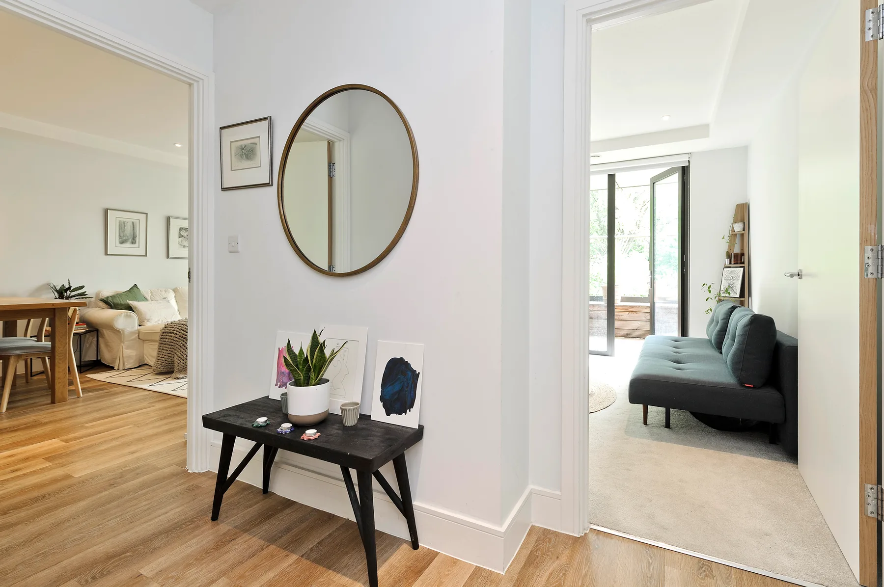 Un pasillo interior luminoso da a una sala con un sofá oscuro y una mesa consola.