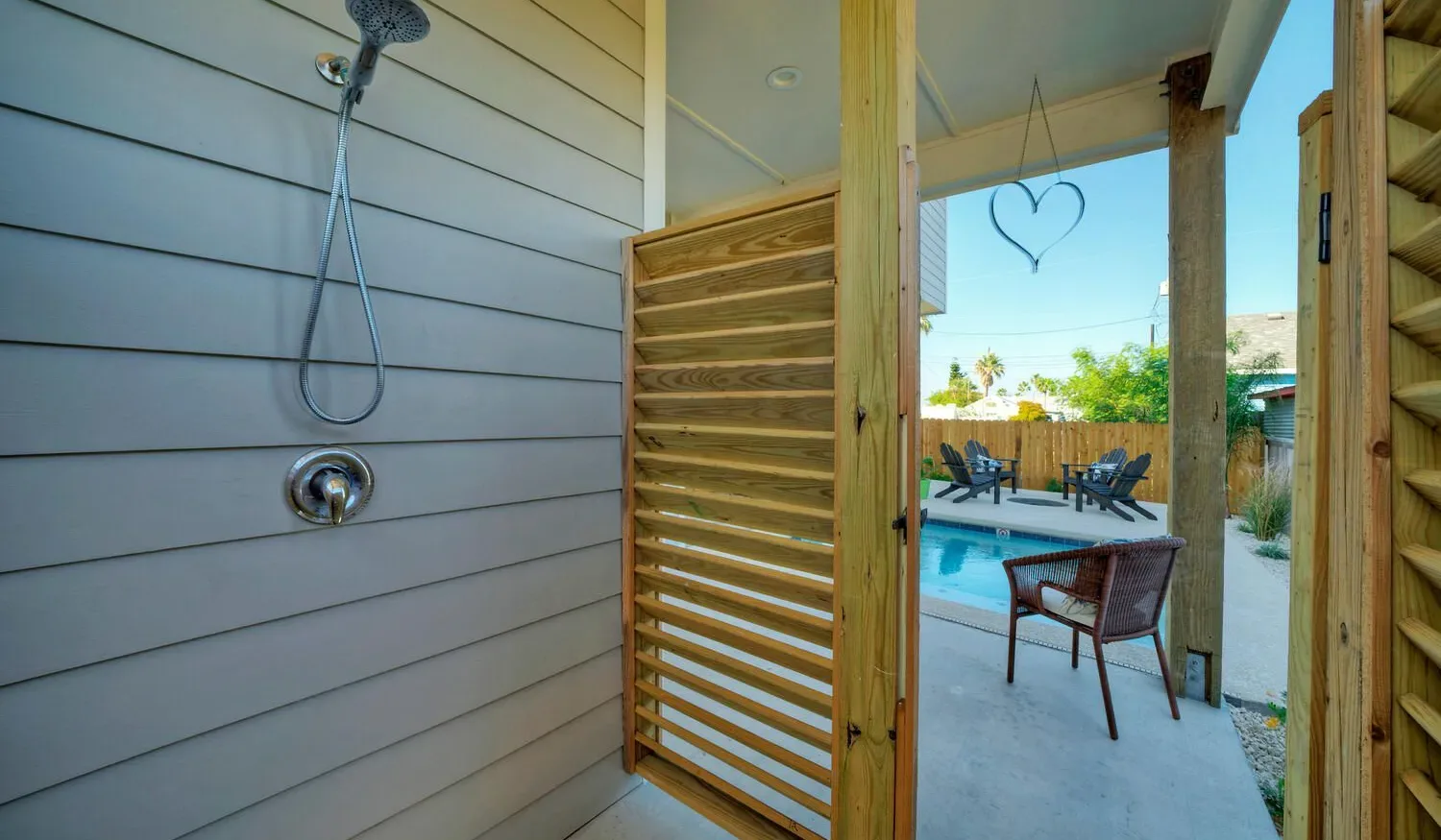 An outdoor shower opens onto a patio with seating and a pool.