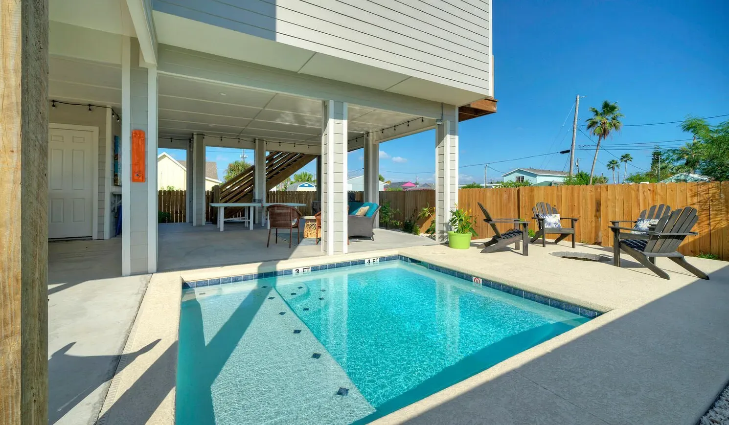 An outdoor swimming pool sits beside a covered patio with seating.