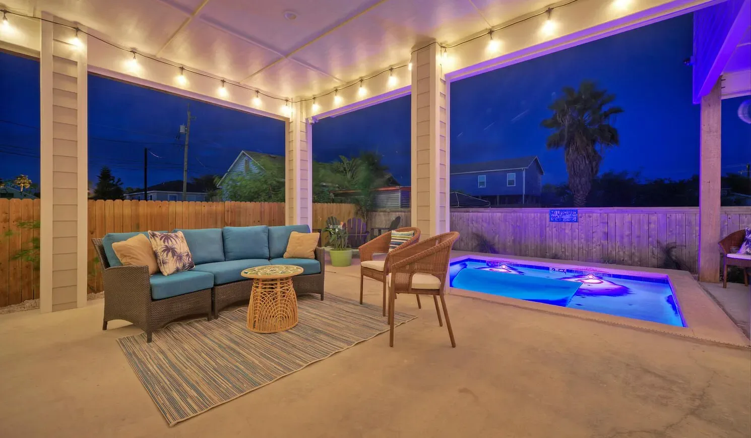 Covered patio seating faces a brightly lit pool beneath string lights.