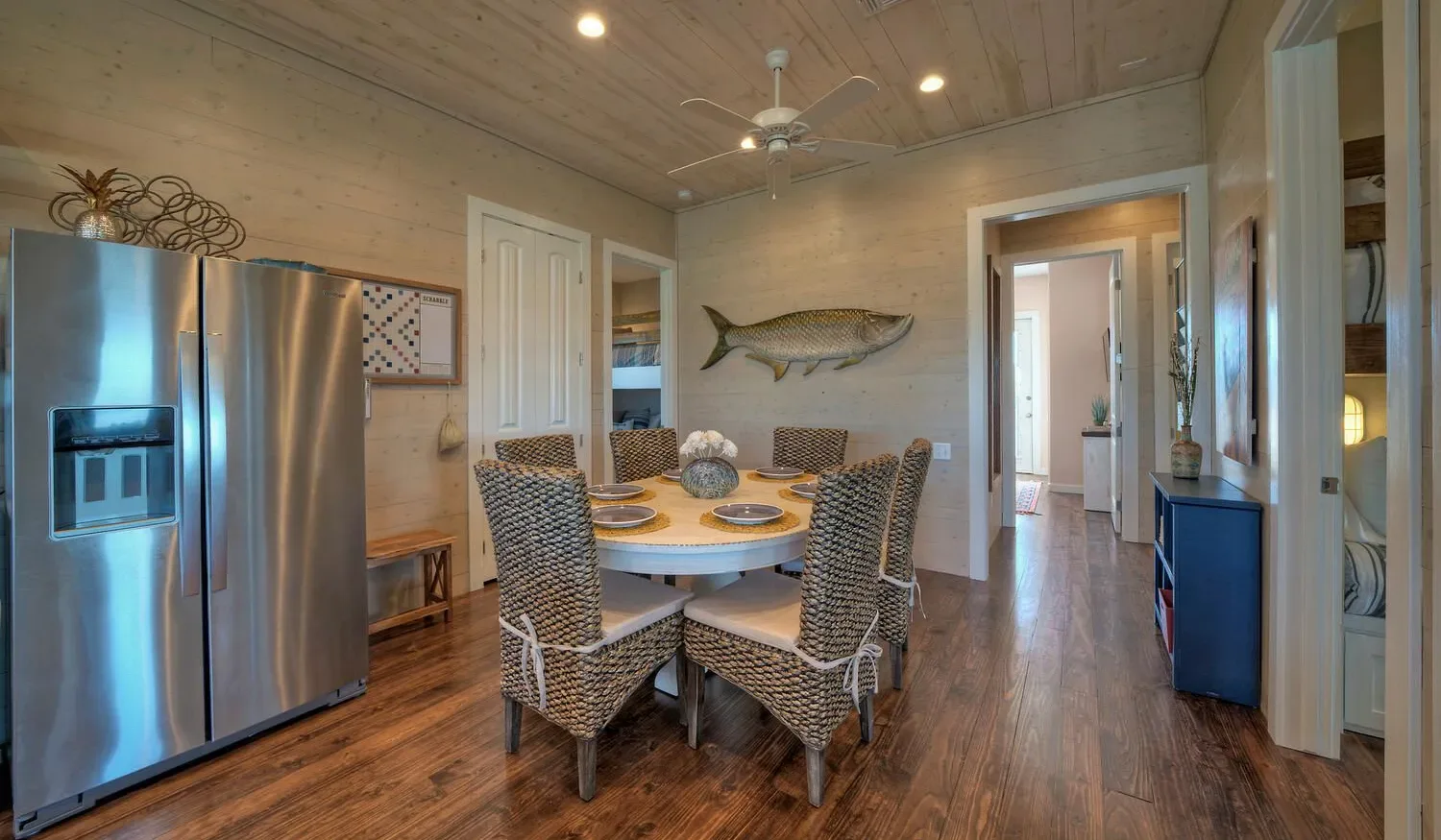 A dining area with a round table and woven chairs sits beside a stainless steel refrigerator.