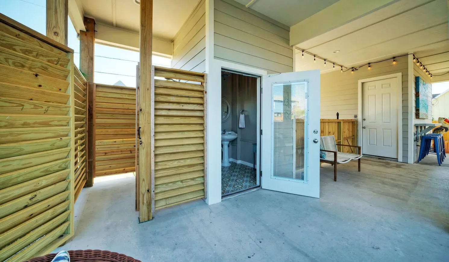 A covered patio with wooden privacy screens and an open bathroom doorway.