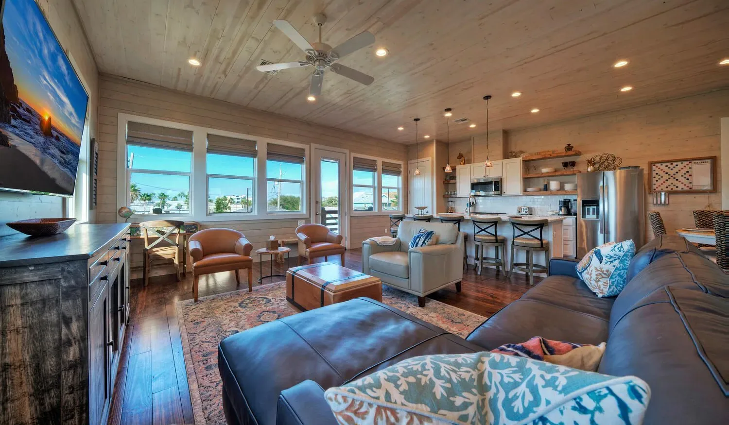 A bright open-plan living room and kitchen with large windows and seating.
