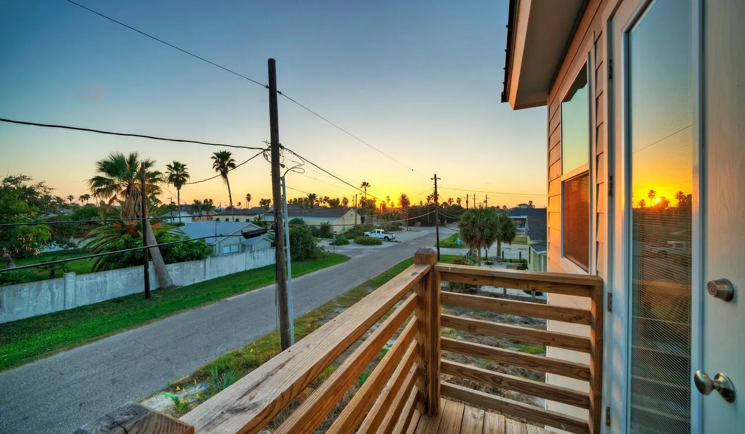 A wooden balcony overlooks a residential street at sunset.