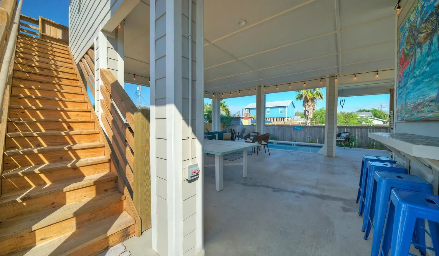 A covered open-air patio with a long table and blue stools.