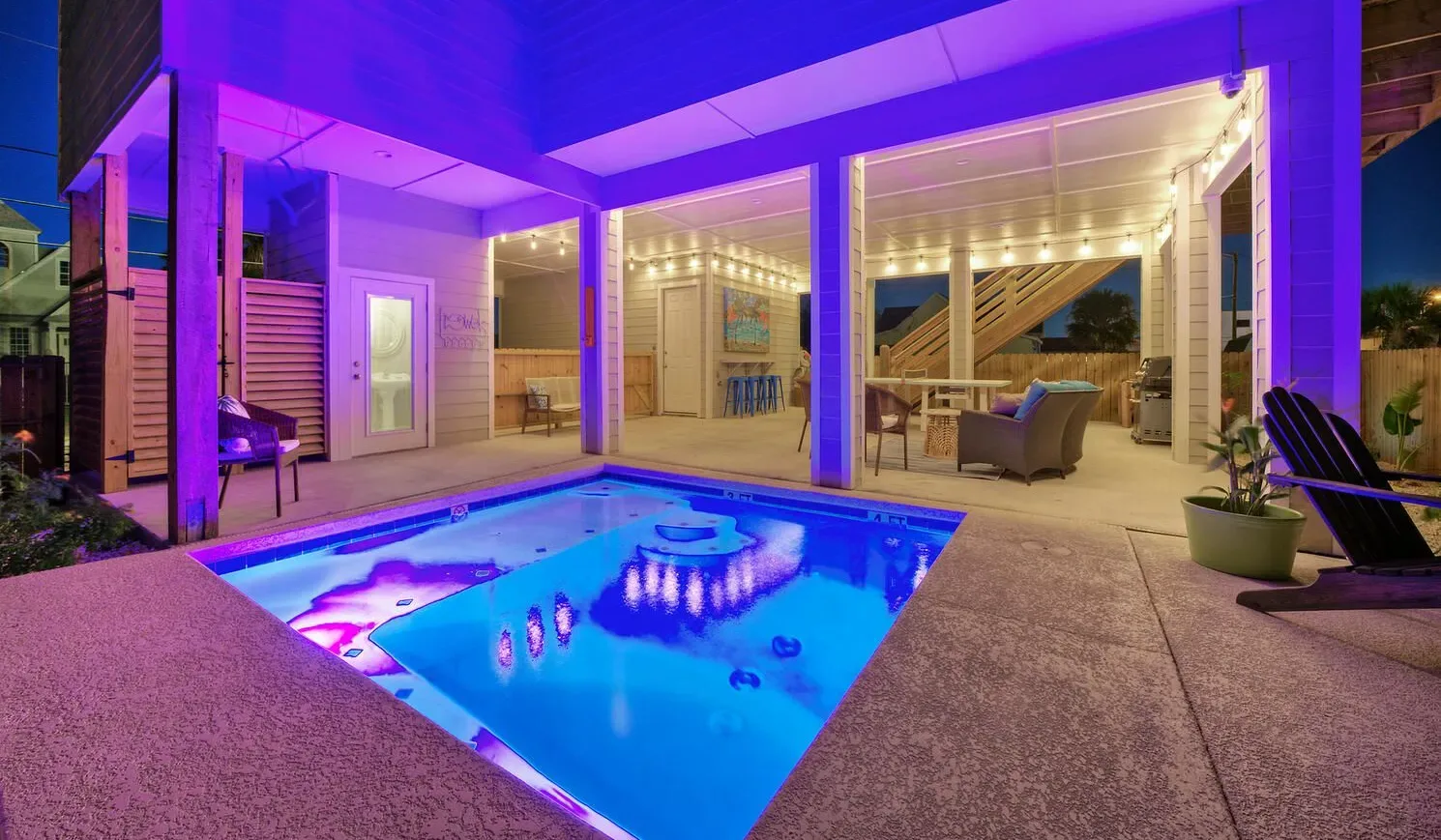 A swimming pool glows beside a covered patio with outdoor seating.