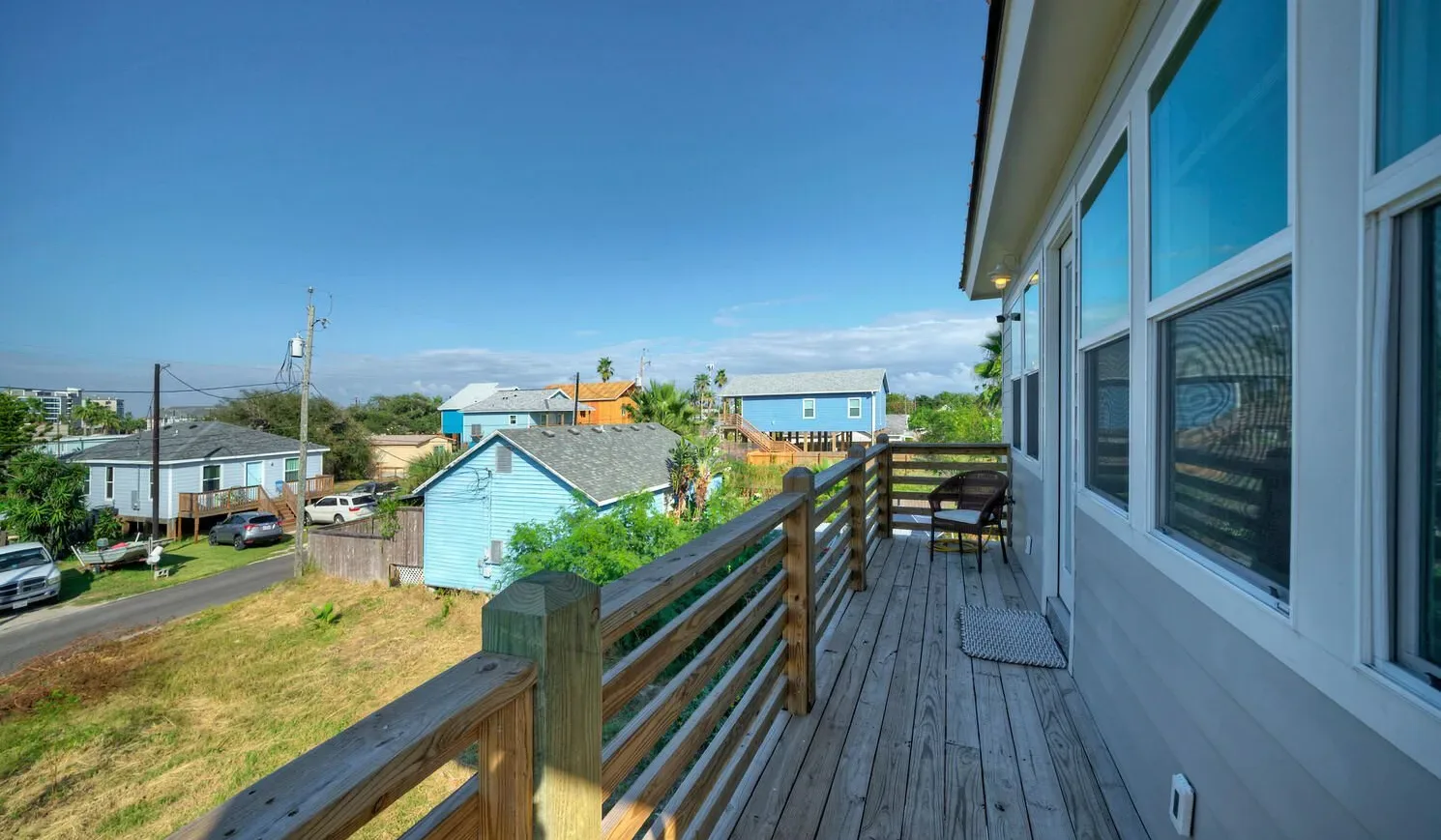 A wooden deck runs alongside a building, overlooking nearby homes and greenery.