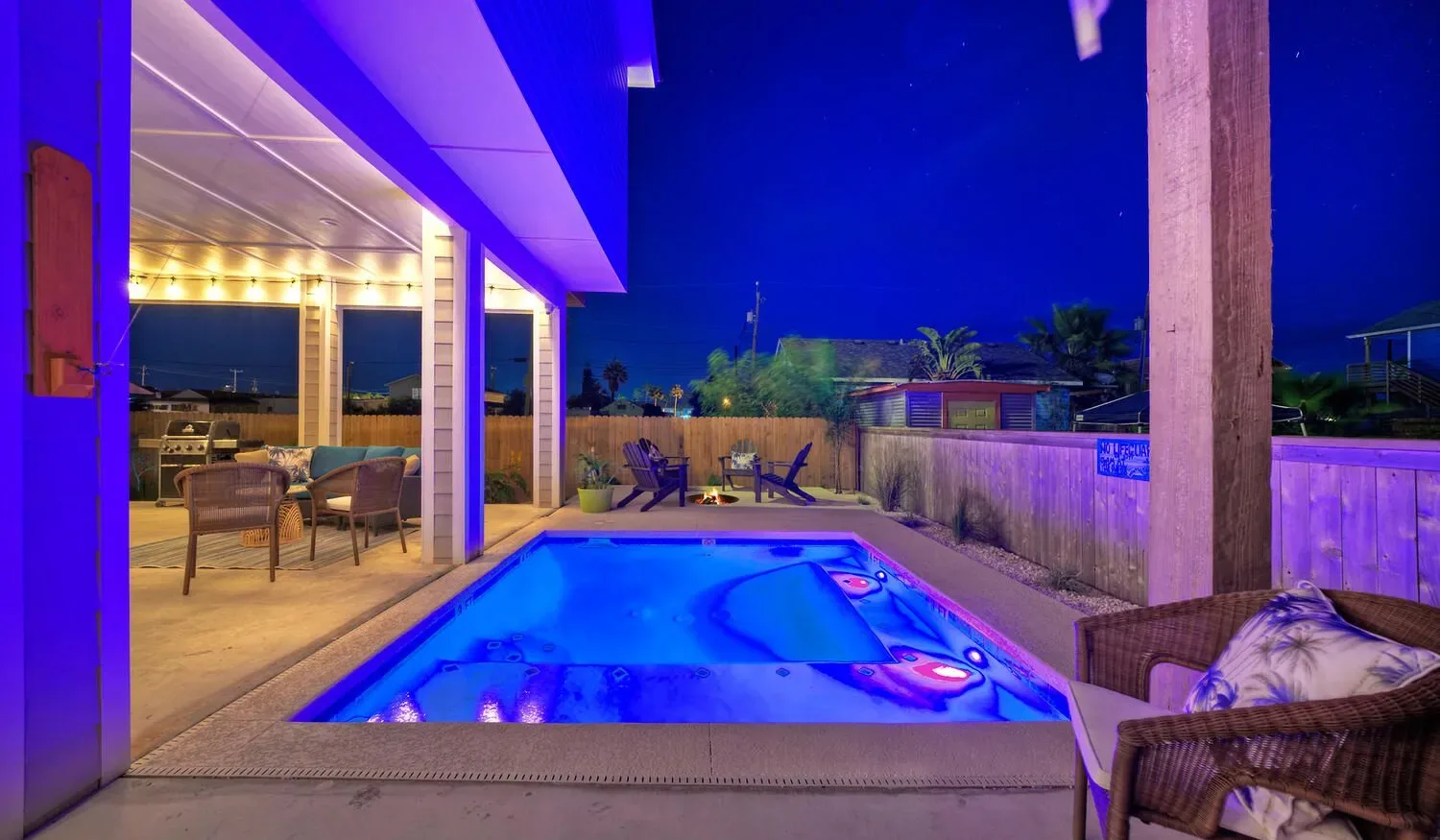 A nighttime patio with a brightly lit swimming pool beside an open seating area.