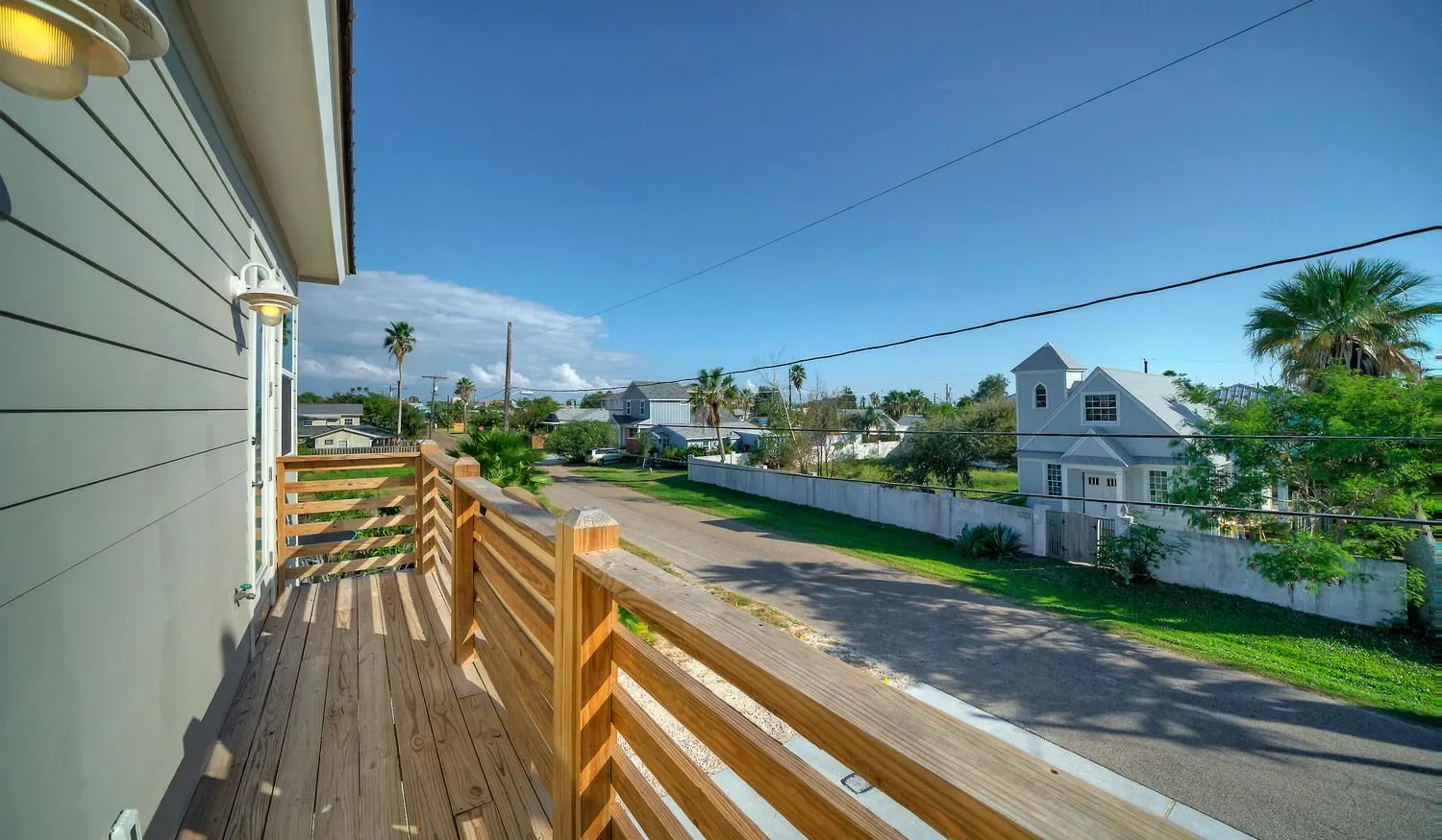 A wooden balcony overlooks a sunny residential street with palm trees.